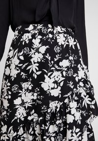 Kukkamekko, jossa on röyhelöhelma, mustalla taustalla ja valkoisilla kukilla. Ressorivyötärö ja kevyt kangas.