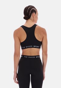 Crni sportski grudnjak s dizajnom u racerback stilu i elastičnom trakom s brandom. Glatka tekstura, minimalistički stil i uska silueta.