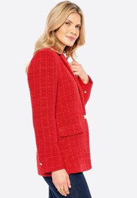 Blazer rosso texturizzato con una trama a reticolo, due tasche frontali e bottoni in tonalità oro. Vestibilità su misura, con revers a scollo.