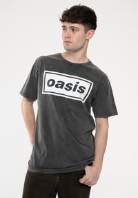 Dark gray cotton t-shirt with short sleeves and a crew neck, featuring a large white rectangular logo that says "oasis" in bold black letters.