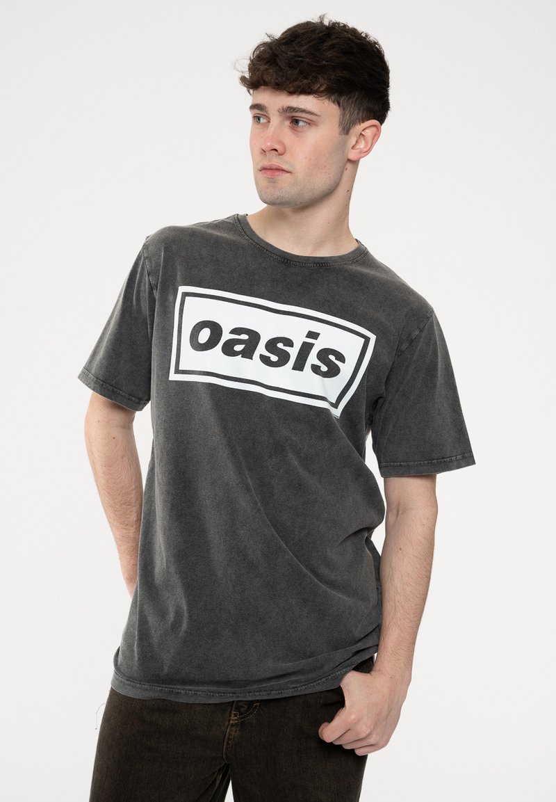 Dark gray cotton t-shirt with short sleeves and a crew neck, featuring a large white rectangular logo that says "oasis" in bold black letters.