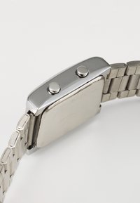 Montre en acier inoxydable argenté avec un boîtier rectangulaire, deux boutons-poussoirs sur le côté et un bracelet métallique à maillons, présentant une finition polie.