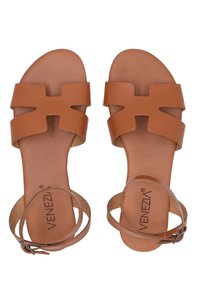 Bruine leren sandalen met brede kruislussen, verstelbare enkelriem en een platte zool. Opvallende merknaam op de binnenzool.