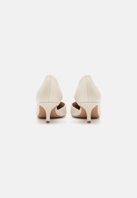 Beige høye hæler med strukturert overflate, spiss tå og utskjæringsdesign. Har en slank hæl for formelle anledninger.
