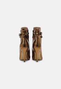 Højhælede ankelstøvler i skinnende metallic bronze slangeskindsprint. Har spænde detaljer ved anklen og en spids tådesign.