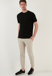 Čierne bavlnené tričko s krátkymi rukávmi; béžové slim-fit nohavice s viditeľným stehovaním; čierne tenisky s jemnými akcentmi.