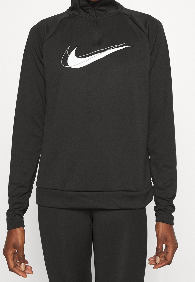 Musta urheilupaita, joka on valmistettu sileästä kankaasta. Siinä on korkea kaulus ja neljännesvetoketju. Rinnassa valkoinen Nike-logon swoosh.