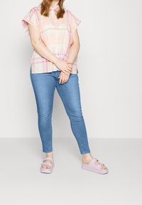 Camisa de cuadros de manga corta en colores pastel, combinada con jeans ajustados azules claros y sandalias de plataforma lavanda con un detalle de lazo.