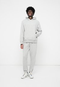 Sweatshirt cinza de algodão com um bolso frontal e calças de moletão a condizer. O modelo usa ténis brancos, exibindo um corte relaxado e um design simples.