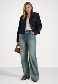 Giacca corta navy con bottoni argentati, canotta bianca, jeans a gamba larga blu sbiaditi, cintura marrone e piccola borsa marrone. Tacchi marroni.