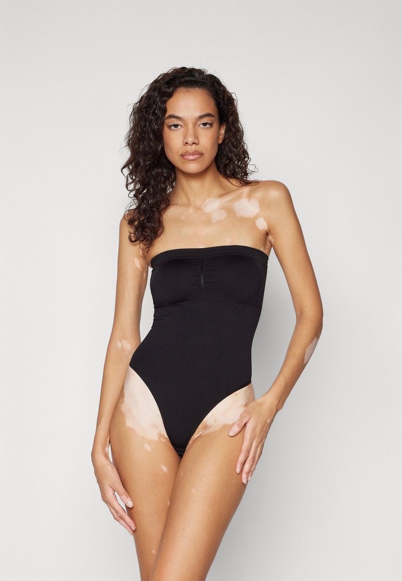 Svart stroppeløs en-delt badedrakt med et tettsittende bodice og høyt kutt på benåpningene. Glatt materiale med en subtil glans og samlet detaljering foran.