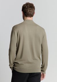 Brede gebreide trui in een licht olijfgroene kleur, met een textured stof en lange mouwen met een geribde zoom en kraag.