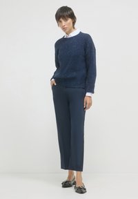 Pullover navy in maglia con tessuto testurizzato, abbinato a pantaloni navy su misura. Mocassini neri con dettagli in hardware decorativo.