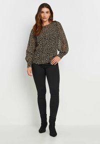 Blusa nera con stampa leopardata, maniche lunghe trasparenti, scollatura arrotondata, abbinata a jeans skinny neri e stivali alla caviglia.