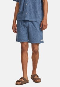 Blue textured shorts with a floral pattern, made of soft fabric. Paired with a matching short-sleeve shirt and brown sandals.