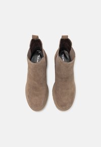 Paire de bottines marron en daim avec languettes de tirage et panneaux latéraux élastiques, vues de dessus sur un fond clair.