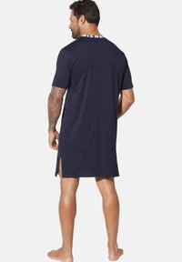 Navy short-sleeve nightshirt with a straight cut, featuring side slits and a contrasting patterned neckline. Soft cotton material.