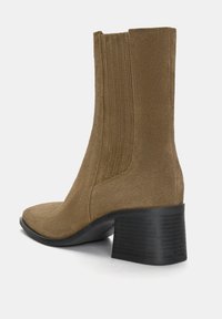 Bottine en daim marron avec un bout pointu, des panneaux latéraux élastiques et un talon noir texturé. Présente un design épuré avec un minimum de détails.