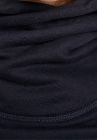 Primissimo piano di strati di tessuto scuro con cuciture visibili, che mostrano la texture e le pieghe di un indumento.