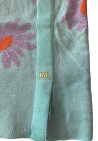 Maglione a maglia turchese chiaro con grandi margherite viola dai centri arancioni, impreziosito da un'etichetta dorata "DYR" e uno spacco laterale.