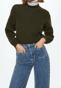 Suéter verde de lana con cuello alto, mangas largas y textura de canalé, combinado con unos jeans de mezclilla azul de cintura alta con bolsillos frontales.