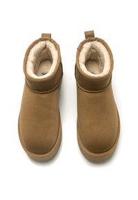 Bottes chelsea en daim marron avec une doublure en laine d'agneau et une conception simple. Elles comportent des coutures renforcées et des languettes pour un enfilage facile.