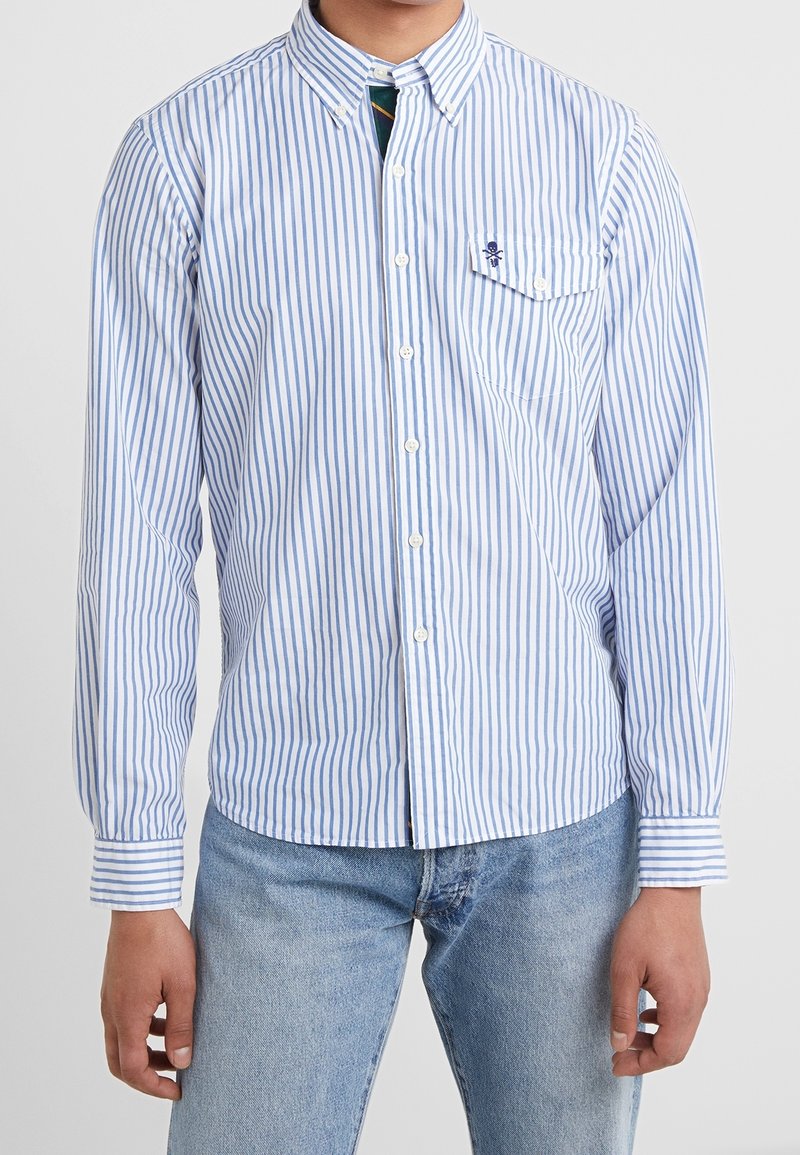 Ljust blå och vit randig skjorta med knappar, med en bröstficka, krage med knappar och lång ärm. Tillverkad av lätt tyg.