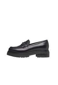 Mocassin en cuir noir avec une semelle en caoutchouc épaisse, des coutures détaillées et une bride décorative traversant le cou-de-pied pour un maintien sûr.