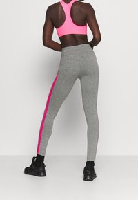 Szare legginsy z różowym paskiem po boku i detalem z logo. Połączone z jasnoróżowym biustonoszem sportowym z plecami w stylu racerback i elastycznym materiałem.