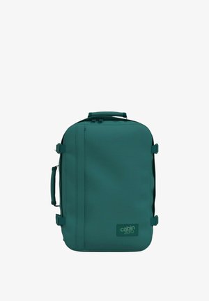 Mochila color teal hecha de tela texturizada con forma rectangular. Presenta correas, un asa superior y un logotipo prominente en la parte delantera.