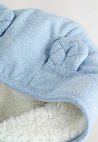 Cappello in pile azzurro chiaro con accenti in tessuto trapuntato sulle orecchie. Fodera interna morbida simile al sherpa, superficie esterna liscia con forma arrotondata.