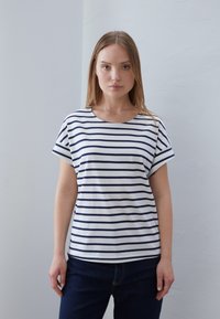 Short-sleeve, crew-neck t-shirt in white with navy horizontal stripes. Soft cotton material, relaxed fit, paired with dark blue jeans.