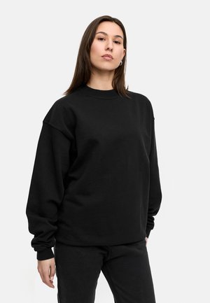 Black oversized sweatshirt with long sleeves and a crew neck, made of a soft, textured fabric; paired with black pants.