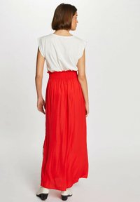 Gonna maxi rossa realizzata in tessuto leggero, con vita arricciata, design fluido e una sottile trama. Abbinata a una maglietta bianca.