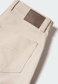 Beige katoenen broek met een gladde textuur, voorzien van een bruine leren label op de tailleband en gestikte details op de achterzakken.