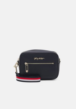 Petit sac bandoulière rectangulaire noir avec fermeture éclair dorée et logo, avec une bandoulière ajustable rayée bleu marine, blanc et rouge.