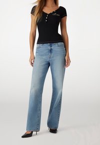 Top negro ajustado con mangas cortas y detalles de botones blancos, combinado con vaqueros de pierna ancha en azul claro. Tacones de aguja negros completan el conjunto.