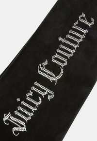 Crni baršunasti materijal s kristalnim ukrasima koji ispisuju "Juicy Couture", koristeći kurziv font. Glatka tekstura, minimalistički dizajn.