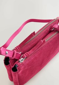 Bolso de ante rosa con dos compartimentos con cremallera, un diseño plano y una correa delgada y ajustable. Presenta herrajes plateados y costuras de acento.