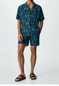 Lyhythihainen paita ja shortsit sinivihreässä kuosissa, jossa abstrakteja muotoja. Valmistettu kevyestä kankaasta, sisältää kauluksen ja taskun.