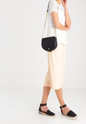 Kvinne iført hvid hæklede top, beige midi-nederdel, sorte ankelstrop espadriller og bærende sort læder crossbody taske med kæde. 
