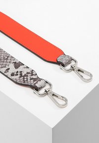 Correa lisa de cuero rojo con detalles de piel de serpiente gris, con herrajes y clips de metal plateado, sobre una superficie blanca.