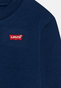 Felpa blu navy con scollo a costine e logo Levi's ricamato in rosso. Tessuto morbido, design aderente, con dettagli sulle maniche.