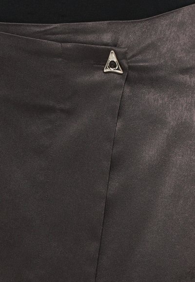 Primer plano de una tela gris oscuro con un broche triangular plateado que sujeta un pliegue superpuesto sobre un material suave.