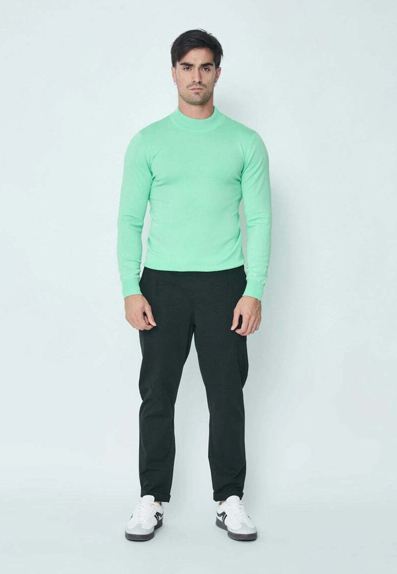 Chemise longue à manches vert menthe, silhouette cintrée, avec un pantalon noir fuselé et des baskets blanches avec des accents gris. Texture douce, design décontracté.