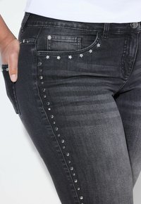 Sorte denimjeans med sølvstjerner og nitter langs siden, med et klassisk fem-lomme design og slim fit.