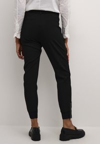 Svarta tapered byxor med en mjuk textur, slankt design och dragkedjor vid anklarna. Kombination med en vit skjorta med volangdetaljer på ärmarna.