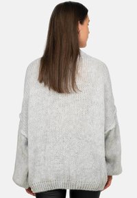 Maglione grigio chiaro, oversize, realizzato in lavorazione a maglia con una texture morbida, spalline scese e orlo a costine. La vista posteriore mostra maniche lunghe e una vestibilità rilassata.