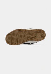 Sneaker featuring a rubber sole with a zigzag pattern, black and white upper, and beige accents on the outsole for grip and support.