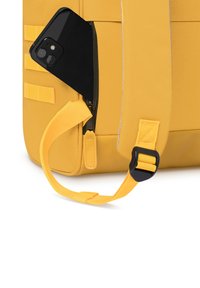 Zaino giallo con una finitura testurizzata, dotato di un telefono nero parzialmente inserito in una tasca con zip e di una tracolla in rete con una fibbia in plastica.